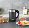 Black electric kettle on a kitchen counter with a plate of food and a cup of tea.