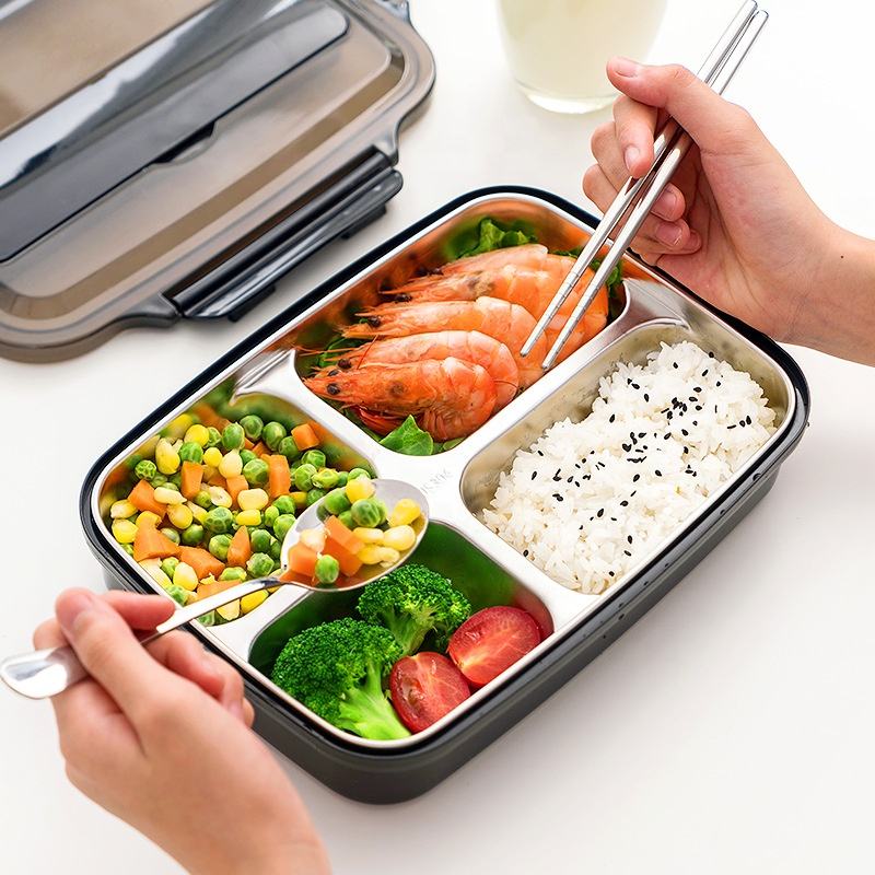 Bento box with compartments of food including shrimp, rice, vegetables, and a hand using chopsticks.